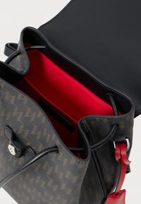 Sac à main à motif marron avec rabat en cuir noir et doublure intérieure rouge, doté d'une fermeture à cordon et d'un détail en bouton argenté.