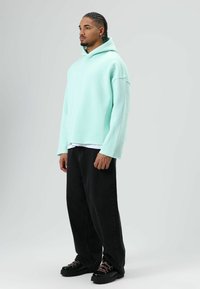 Sweat à capuche surdimensionné vert menthe avec une poche kangourou, superposé à un t-shirt blanc ; associé à un jean large noir et des bottes noires.