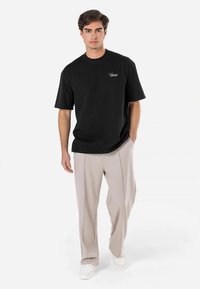 Svart bomullst-shirt med korta ärmar och rund halsringning, har en liten vit logotyp på bröstet. Matchas med beige byxor och vita sneakers.