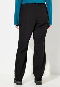Black elastic-waist pants with tapered cuffs, featuring a smooth texture and casual design. Worn with a blue long-sleeve top.