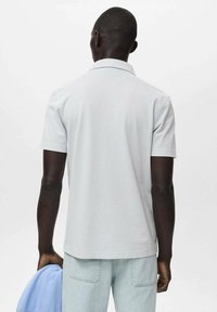 Ljust grå pikétröja med korta ärmar, krage och slät yta, i ena handen håller jag ljusblå byxor i mjukisdress.