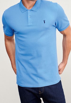 Polo bleu en coton avec un col à trois boutons, des manches courtes et un petit logo de homard en bleu foncé sur la poitrine.