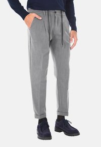 Pantaloni grigi su misura con pieghe, vita elasticizzata, coulisse e tasche laterali. Abbinati a scarpe scure e a una maglia blu navy.