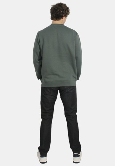 Felpa grigia con scollo rotondo, abbinata a jeans di denim scuro. L'outfit presenta una vestibilità comoda e una consistenza morbida, senza motivi visibili.