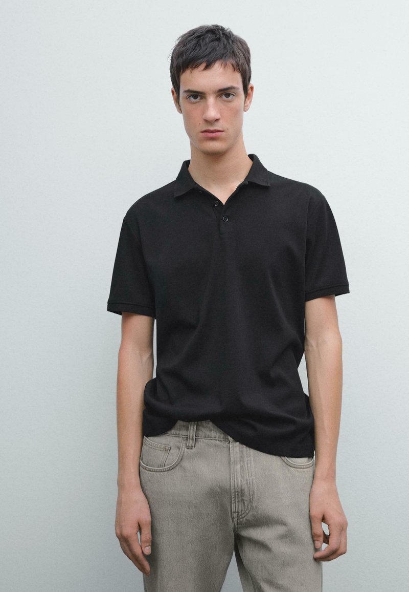 Sort polo shirt med krave og tre-knaps lukning, parret med lysegrå jeans. Glat tekstur; tætsiddende design.