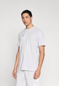 Ανοιχτό γκρι T-shirt από απαλό υλικό, με στρογγυλή λαιμόκοψη, κοντά μανίκια και διακριτικό λογότυπο Adidas σε πιο σκούρο γκρι.