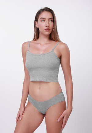 Νεαρή γυναίκα που φοράει γκρι ριγωτό ασορτί τοπ και εσώρουχα, στέκεται με τα χέρια στα πλάγια, κοιτάζοντας προς τα δεξιά της, σε λευκό φόντο.