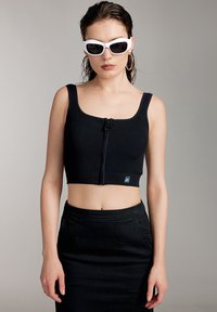 Top cropped nero a coste con zip frontale, abbinato a una gonna nera. Presenta spalline larghe e un'etichetta logo all'orlo.
