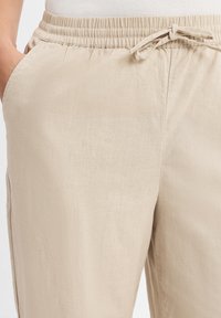 Beige, lichtgewicht broeken met een elastische tailleband en trekkoord. Voorzien van zijzakken en een gladde textuur. Casual ontwerp geschikt voor dagelijks draag.