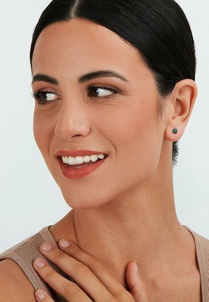 Runde Steckerohrringe mit einem Türkisstein, getragen am Ohr eines Models, das glattes Metall zeigt und eine Nahaufnahme der Gesichtszüge präsentiert.