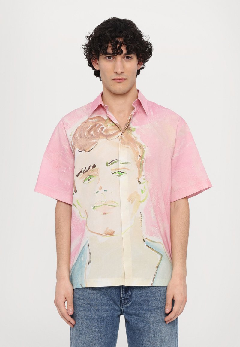 Camisa de manga corta con un fondo rosa y un diseño de cara pintado a mano. Hecha de tela ligera, con botones en la parte delantera y un corte relajado.
