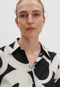 Camicia a fantasia bianco e nero con colletto, bottoni e un mix di forme audaci. Realizzata in tessuto leggero con una texture morbida.