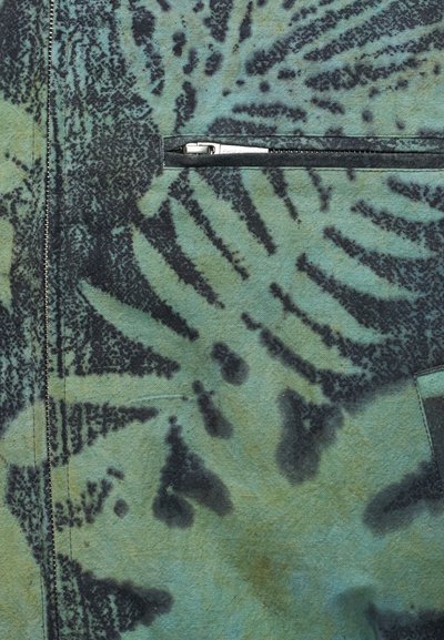 Πράσινο ύφασμα με μαύρο αφηρημένο σχέδιο και κλειστό οριζόντιο φερμουάρ ραμμένο στο υλικό.