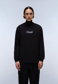 Fekete hosszú ujjú póló, melyen hímzett "Nayajiri" felirat található a mellrészen. Az anyag puhanak tűnik, lazán illeszkedik, és kerek nyakkivágása van.