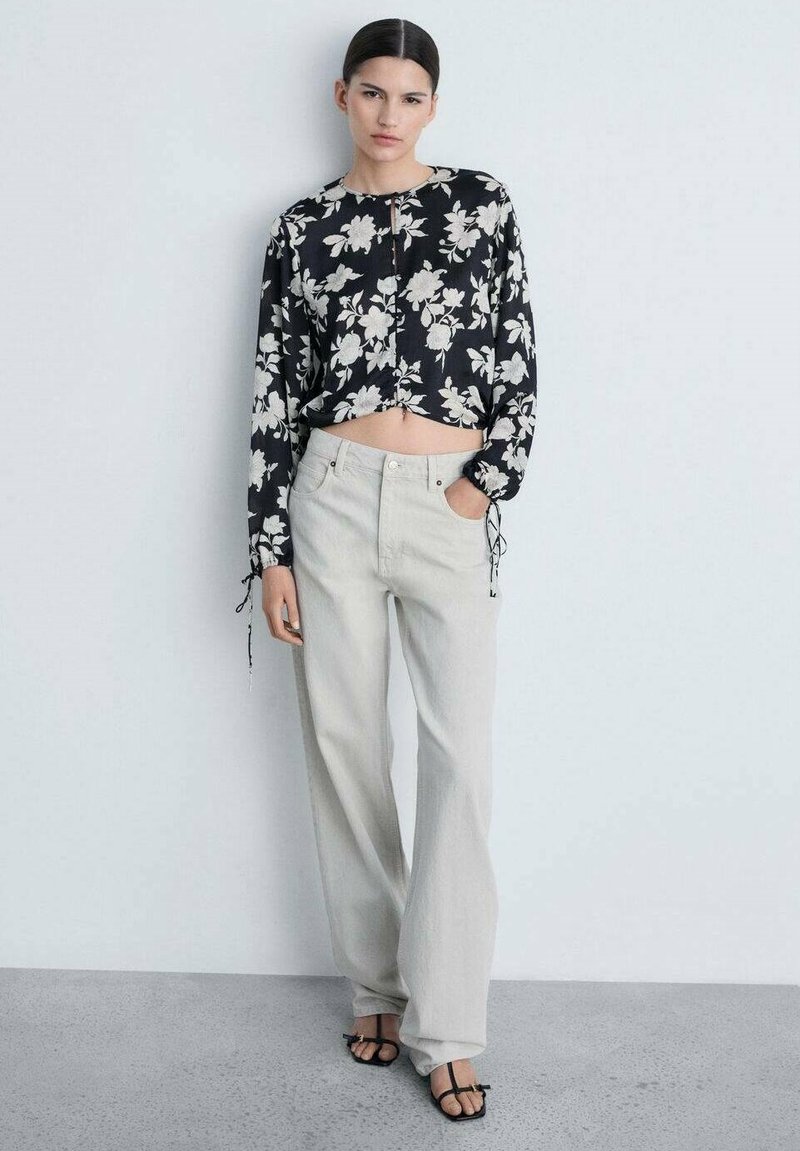 Črn cvetlični crop top z dolgimi rokavi in detajli z vrvicami, v kombinaciji s svetlo sivo širokimi hlačami. Obleka ima sproščen kroj.
