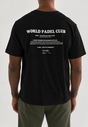 Mand iført en sort t-shirt med hvid tekst, der promoverer World Padel Club og dets fordele for sundhed, fællesskab og moderne livsstil.