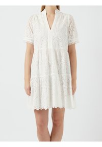 Vit bomullsklänning med hålbroderi, lagerdesign, korta ärmar, scalloped nederkant och en halsringning med en partiell knappslå.