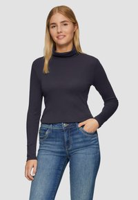 Dunkelblaues Rollkragenoberteil mit langen Ärmeln aus glattem Stoff, kombiniert mit hellblauen Jeans im klassischen Stil und mit Fünf-Taschen-Design.