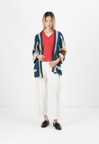Tenue décontractée comprenant un kimono oversized à motifs en bleu marine, une chemise rouge à boutons, un pantalon large blanc et des chaussures noires.