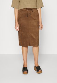 Jupe en suede marron avec une taille à cordon de serrage, dotée d'une coupe droite et d'un détail fente. Associée à des sabots noirs à bout ouvert et un pull texturé.