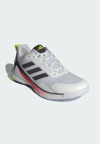 Chaussure de sport grise avec empeigne en maille, accents noirs, languette de talon verte et semelle rouge. Comprend un design à trois rayures noires et des surfaces texturées.