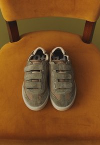 Paire de baskets grises à scratch posées sur une chaise orange rembourrée avec des accoudoirs en bois.
