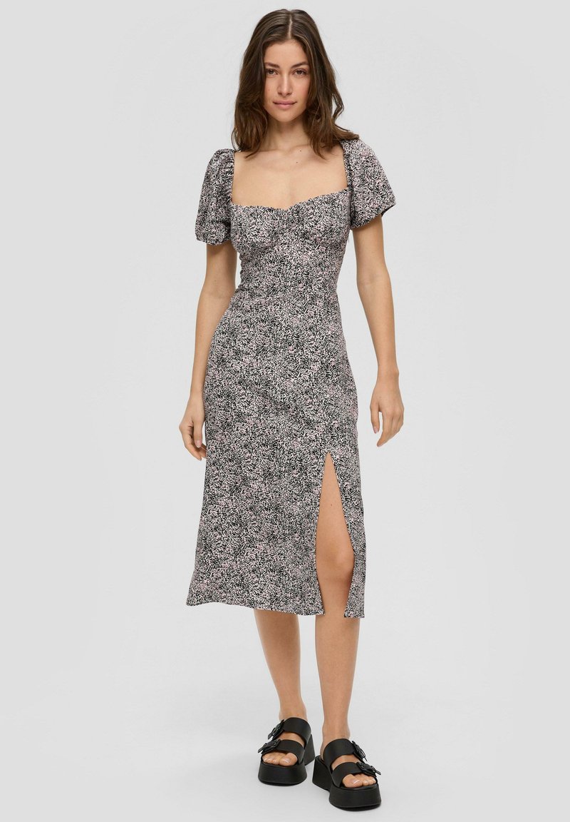 Robe midi florale en noir, rose et blanc. Manches bouffantes, décolleté carré, coupe slim avec fente sur le côté, et tissu léger. Sandales à plateforme noires.