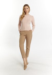 Helles rosa strukturiertes Strickpullover mit langen Ärmeln, kombiniert mit beigen maßgeschneiderten Hosen und braunen Slippern, die eine figurbetonte Silhouette zeigen.