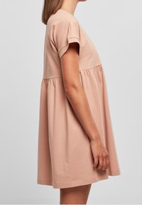 Kurzärmeliges, hellrosa Kleid aus weichem Baumwollstoff; hat einen taillierten Oberteil mit einem ausgestellten, gerafften Rock und zarten Saumnähten.