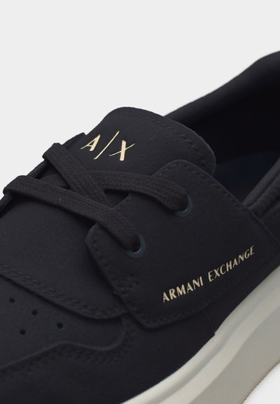 Baskets noires Armani Exchange avec lacets noirs, "A|X" sur la languette et "ARMANI EXCHANGE" imprimé en or sur le côté.