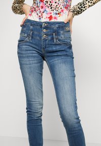 Jeans in denim blu con design a vita alta, dotati di chiusura con tre bottoni, tasche anteriori e vestibilità slim. Leggera scoloritura nella zona delle cosce.