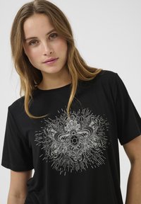 T-shirt nera realizzata in morbido tessuto, con un dettagliato design grafico argento caratterizzato da motivi intricati e linee che si irradiano al centro.