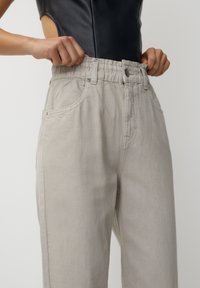 Pantalons taille haute gris clair avec une taille élastique, deux poches latérales et une texture lisse. Pas de fermetures visibles.