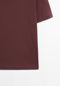 Bordeauxrotes Baumwoll-T-Shirt mit kurzen Ärmeln, ausgestattet mit einem Rundhalsausschnitt und einer glatten Oberfläche. Der Saum ist mit einer geraden, sauberen Naht genäht.
