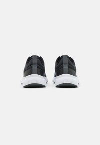 Czarne buty sportowe z fakturowaną siateczkową cholewką, białą podeszwą i pętelką z tyłu; charakteryzujące się smukłym, aerodynamicznym designem.