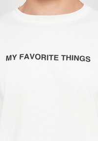 Fehér póló, amelyen vastag fekete betűkkel olvasható, hogy "KEDVENC DOLGAIM" a mellkason. Simább textúrával, klasszikus kerek nyakkivágással.