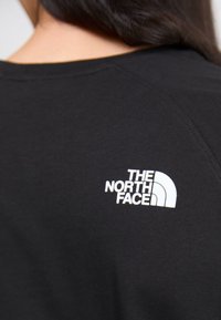 Camiseta de algodón negra con un logo blanco de "The North Face" en la parte superior de la espalda, con un escote redondeado y mangas cortas.