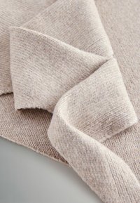 Beez värvi kootud kangas tekstuuriga mustriga, millel on volditud osa, mis loob pehmeid, nähtavaid kõveraid ja siledat viimistlust.