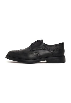 Scarpa brogue in pelle nera con chiusura frontale con lacci, motivi decorativi traforati e tacco basso impilato, vista laterale su sfondo bianco.