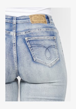 Hellblaue Jeans aus Denim mit einer abgenutzten Optik, ausgestattet mit einem beigefarbenen Lederpatch an der Taille und bestickten Akzenten auf den Gesäßtaschen.