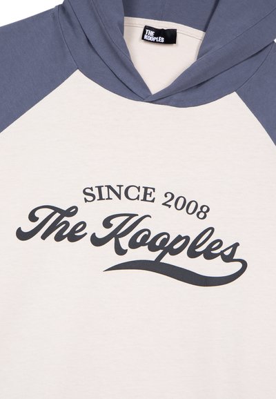 Felpa con cappuccio di colore crema con maniche raglan navy. Presenta la scritta "Dal 2008 The Kooples" stampata in nero, con una texture liscia.