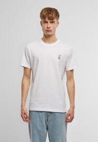 Vit bomulls t-shirt med en liten, färgglad drycksgrafik på vänstra bröstet. Korta ärmar och rundad halsringning. Mjuk textur.