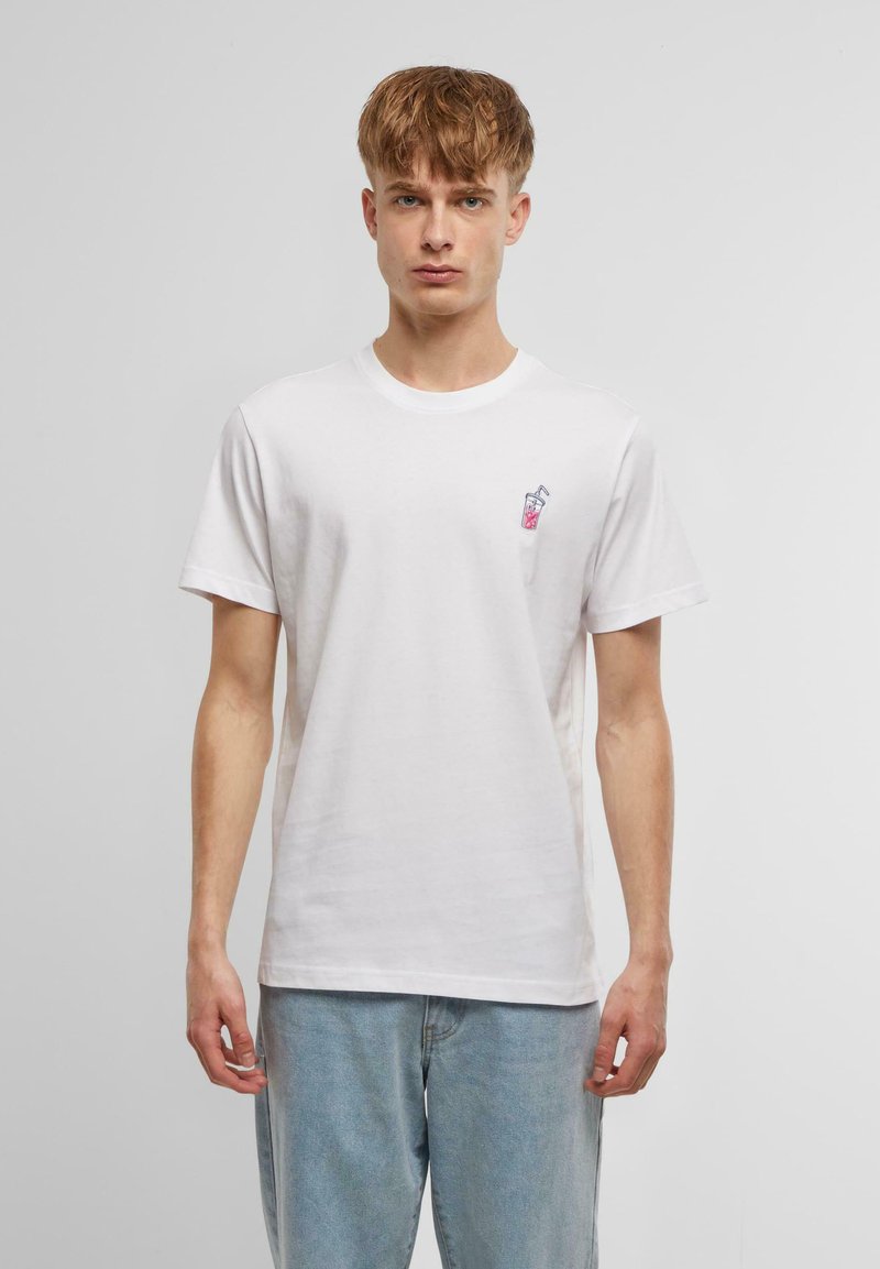 Vit bomulls t-shirt med en liten, färgglad drycksgrafik på vänstra bröstet. Korta ärmar och rundad halsringning. Mjuk textur.