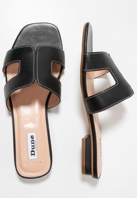 Black leather slide sandals with two wide straps featuring cut-out designs, a square toe, and a low block heel. Contrasting beige insole.