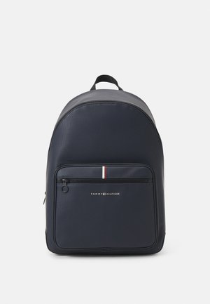 Laivastonsininen reppu, jossa on etutasku vetoketjulla ja pieni punainen, valkoinen ja sininen raita Tommy Hilfigerin logon yläpuolella.