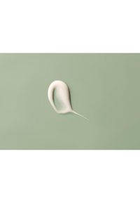 Crème ou lotion blanche en forme lisse et courbée sur un fond vert pastel, avec une pointe et une texture légèrement brillante.