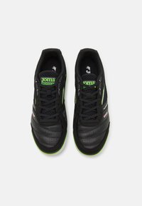 Chaussures de sport noires avec des accents verts, dotées d'une tige en mesh, de détails perforés et d'une semelle plate. Les lacets sont noirs avec une finition lisse.