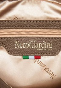 Interno in pelle marrone testurizzata che mostra una tasca con zip, il logo del marchio dorato "NeroGiardini" e un'etichetta con la bandiera italiana.