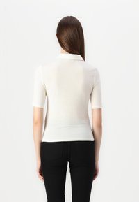 Korte ermer, hvit polo-skjorte laget av mykt stoff. Har en klassisk krage og en slim-fit design. Bæres med svarte slim-fit bukser.