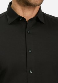 Zwarte button-up shirt met een gladde textuur, lange mouwen en een klassieke kraag met contrasterende zwarte knopen aan de voorkant.